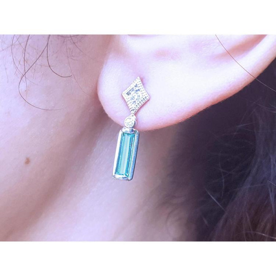 14K white gold emerald baguette and diamond stud earrings on an ear.