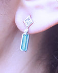 Close-up of a diamond and natural emerald earring on an ear.