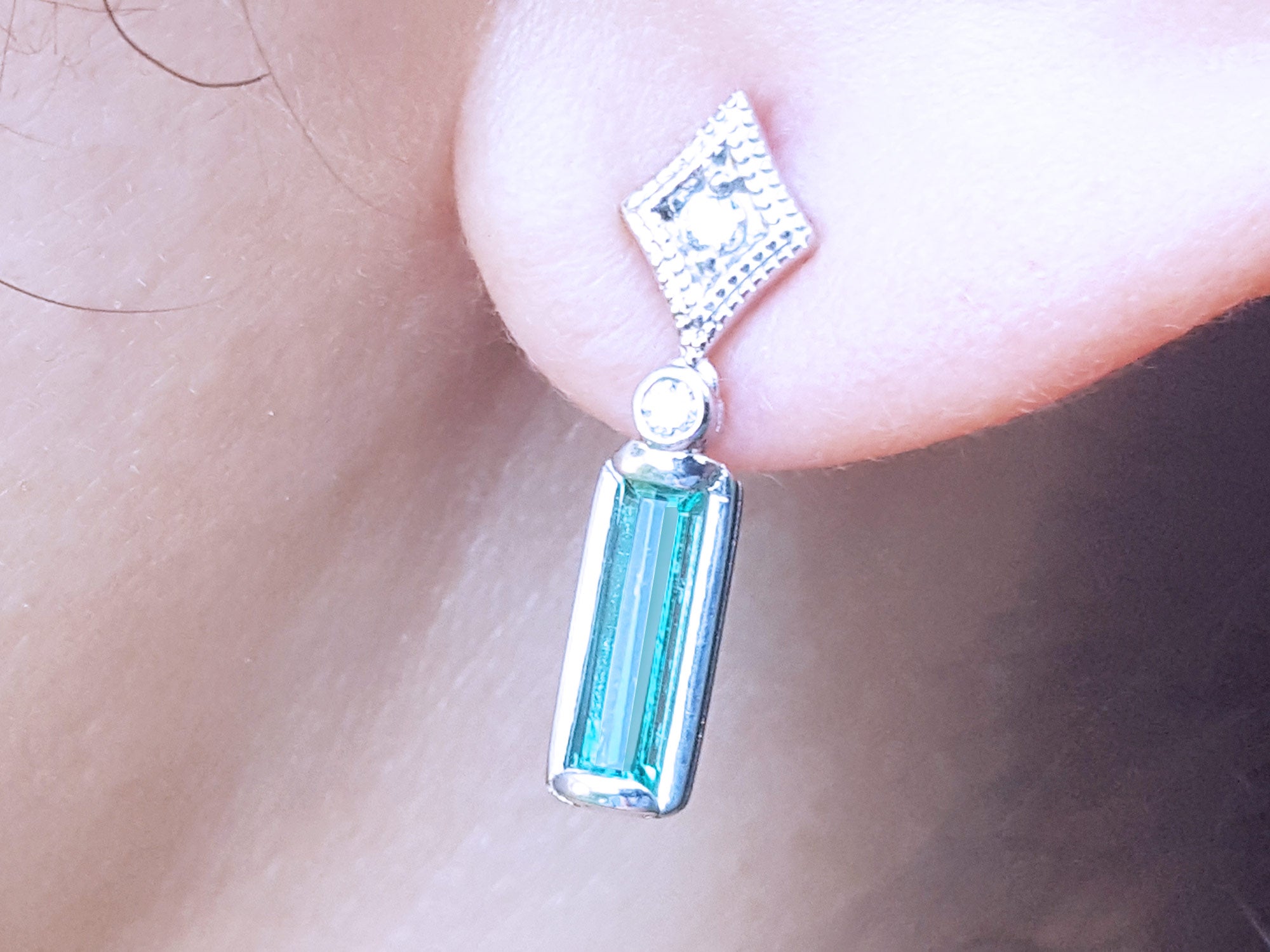 Close-up of a white gold emerald earring with accent diamonds worn on an ear.