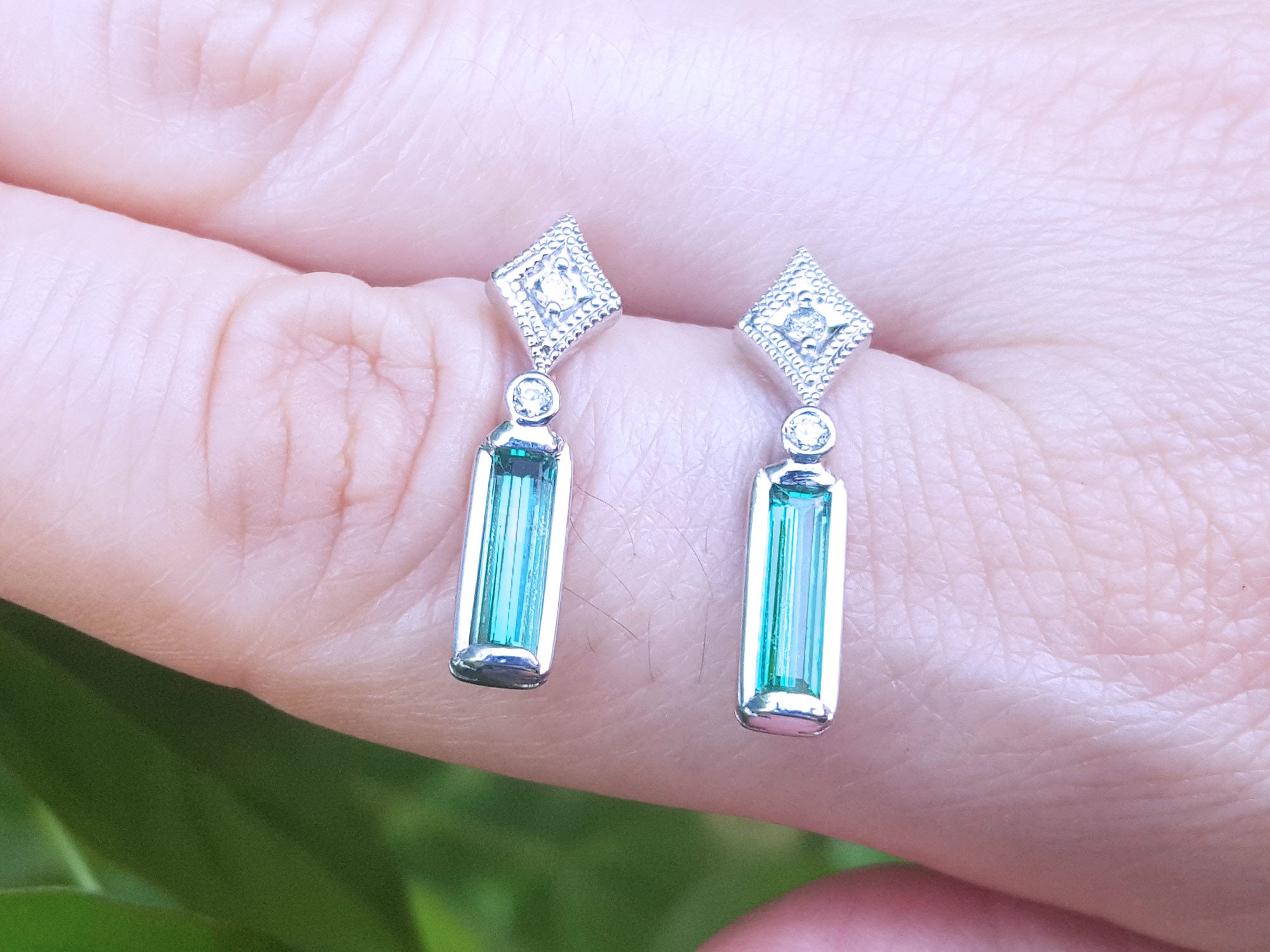 Pair of emerald white gold earrings held between fingers against a blurred background