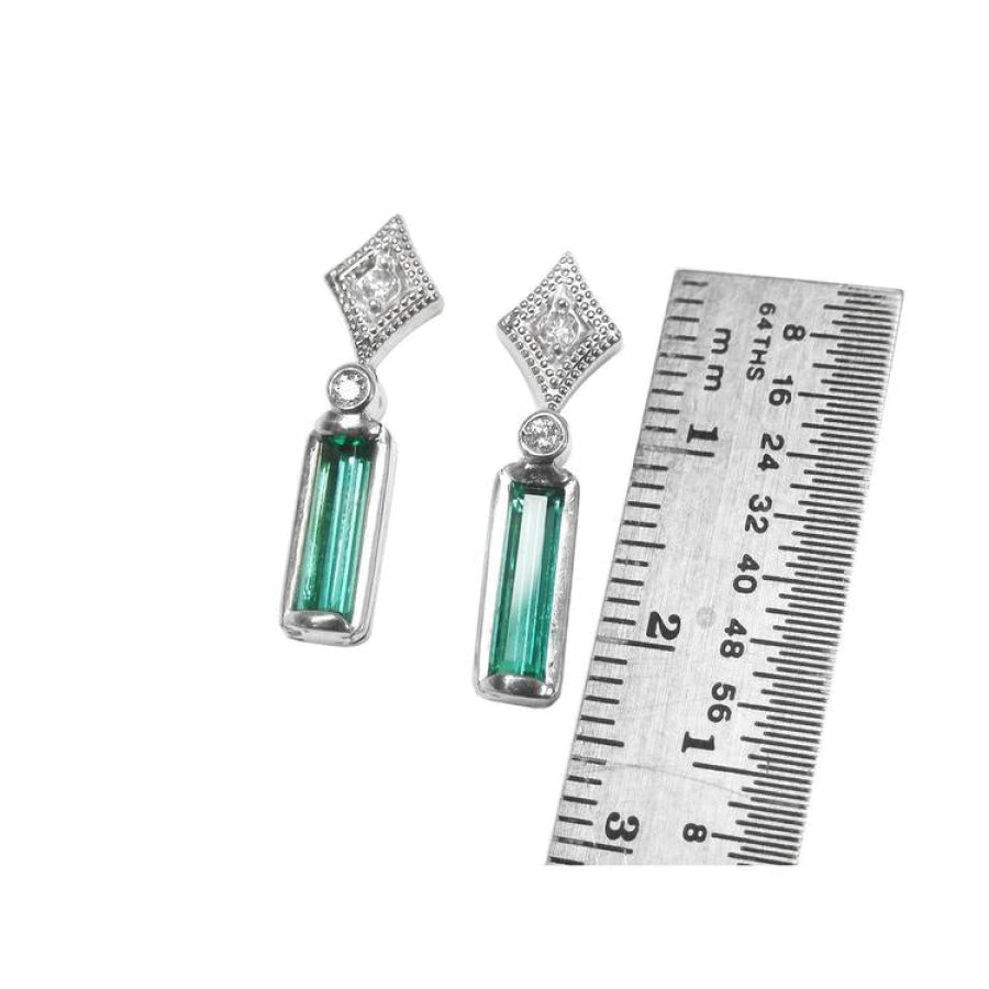 Emerald baguette cut earrings with diamond studs in 14K white gold, next to a ruler for scale.