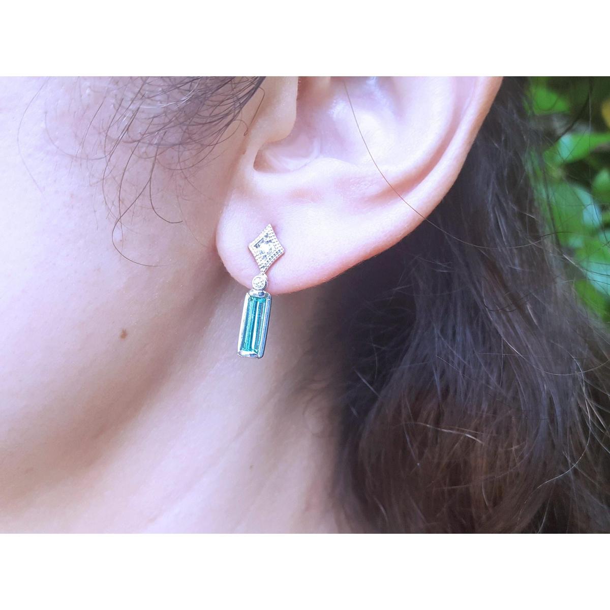 Close-up of an ear wearing a diamond and emerald earring with blurred background