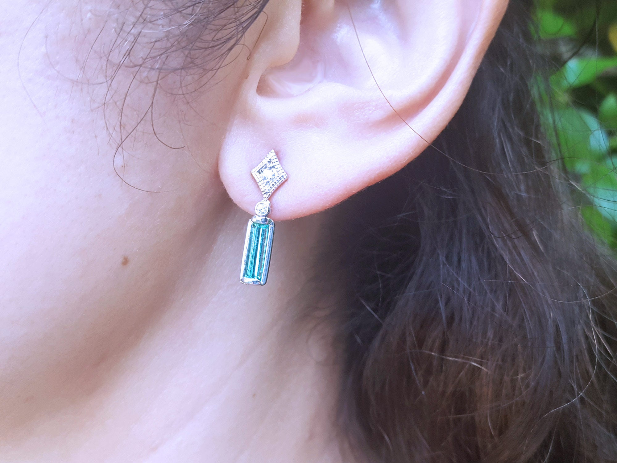 Close-up of an ear wearing a diamond and emerald earring with blurred background