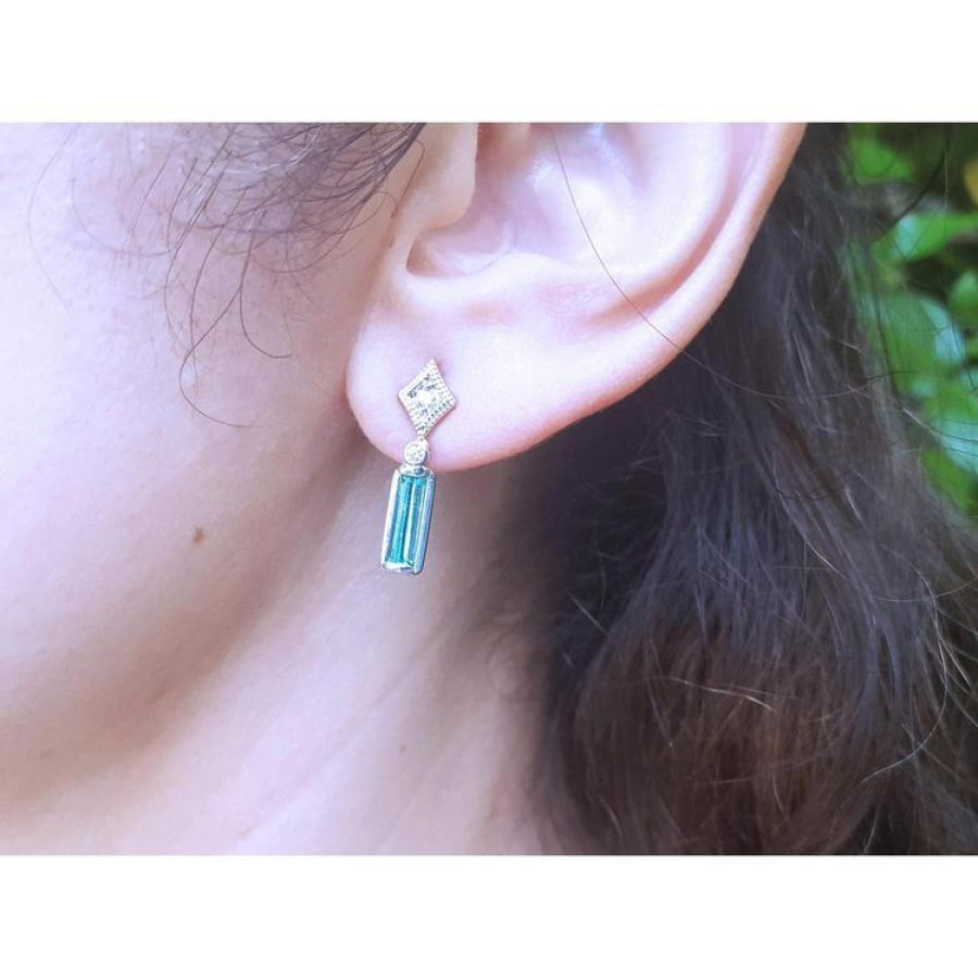 14K white gold emerald baguette cut earrings with diamond studs on an ear.