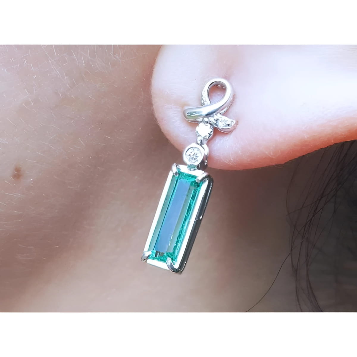 Natural baguette cut emerald earring with a top ribbon-like worn by a person