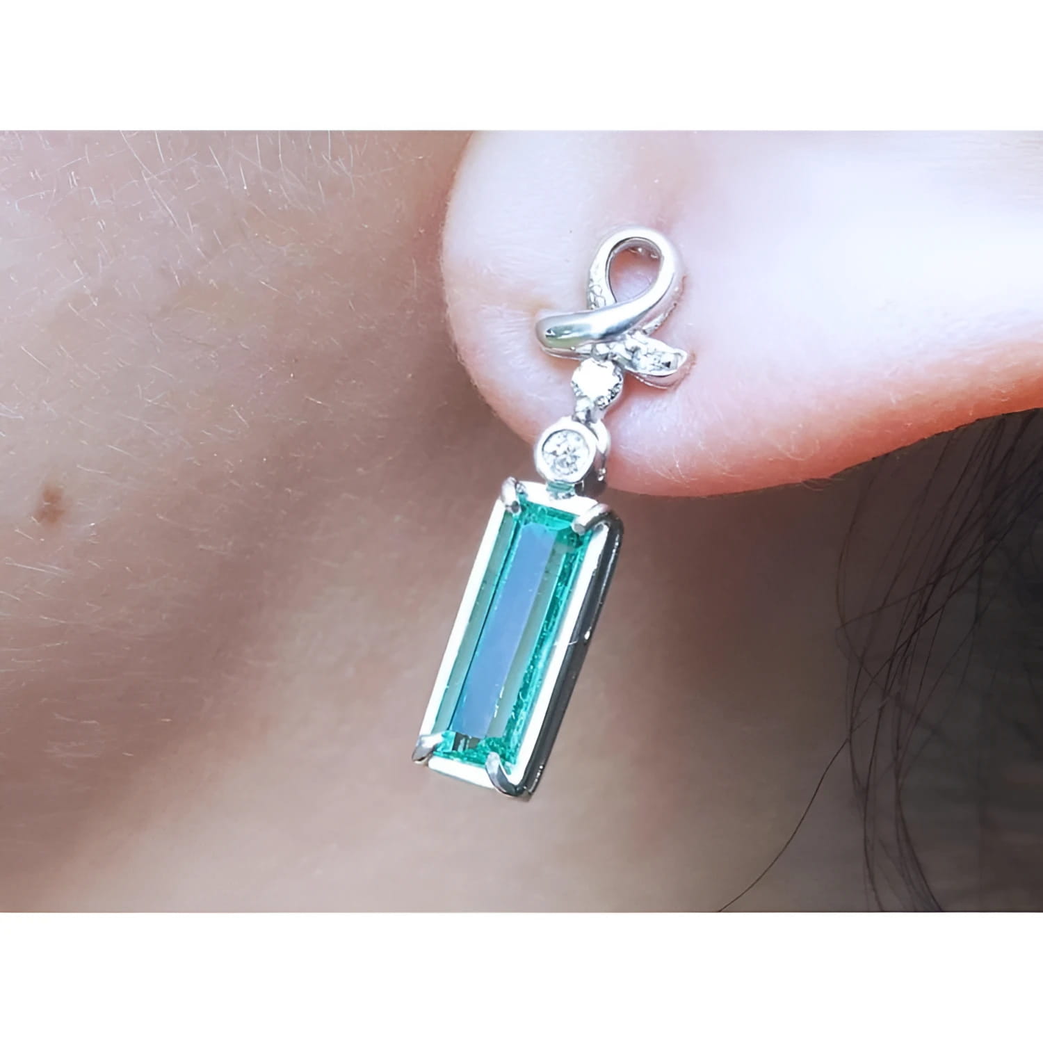 Natural baguette cut emerald earring with a top ribbon-like worn by a person