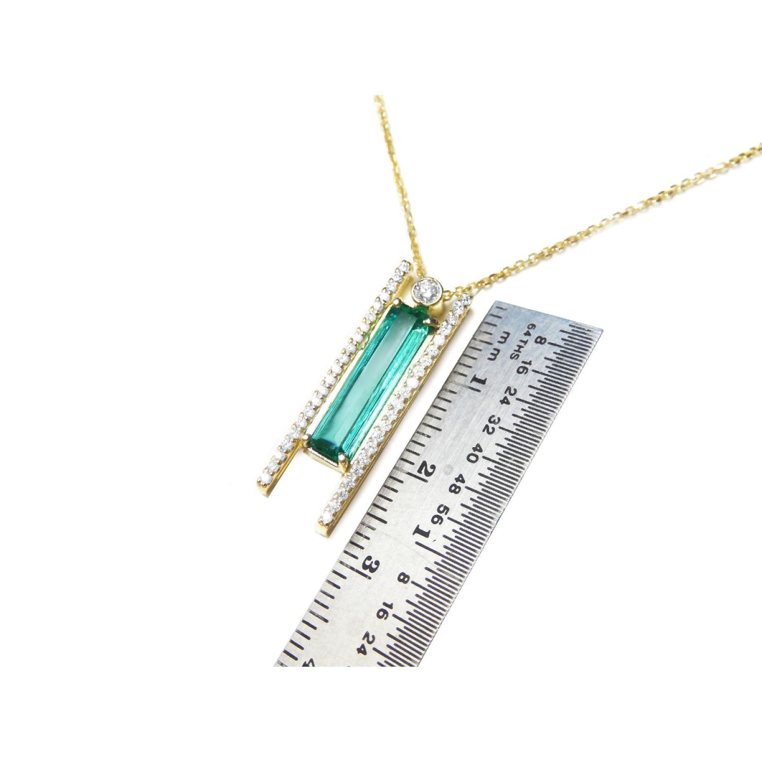 14K yellow gold necklace with a baguette-cut emerald, accent diamonds, and a sliding tube bail, shown next to a metal ruler for scale.