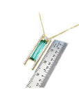 14K yellow gold necklace with a baguette-cut emerald, accent diamonds, and a sliding tube bail, shown next to a metal ruler for scale.