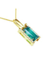 Baguette cut Colombian emerald pendant in 18K yellow gold with diamond accents on a delicate chain.