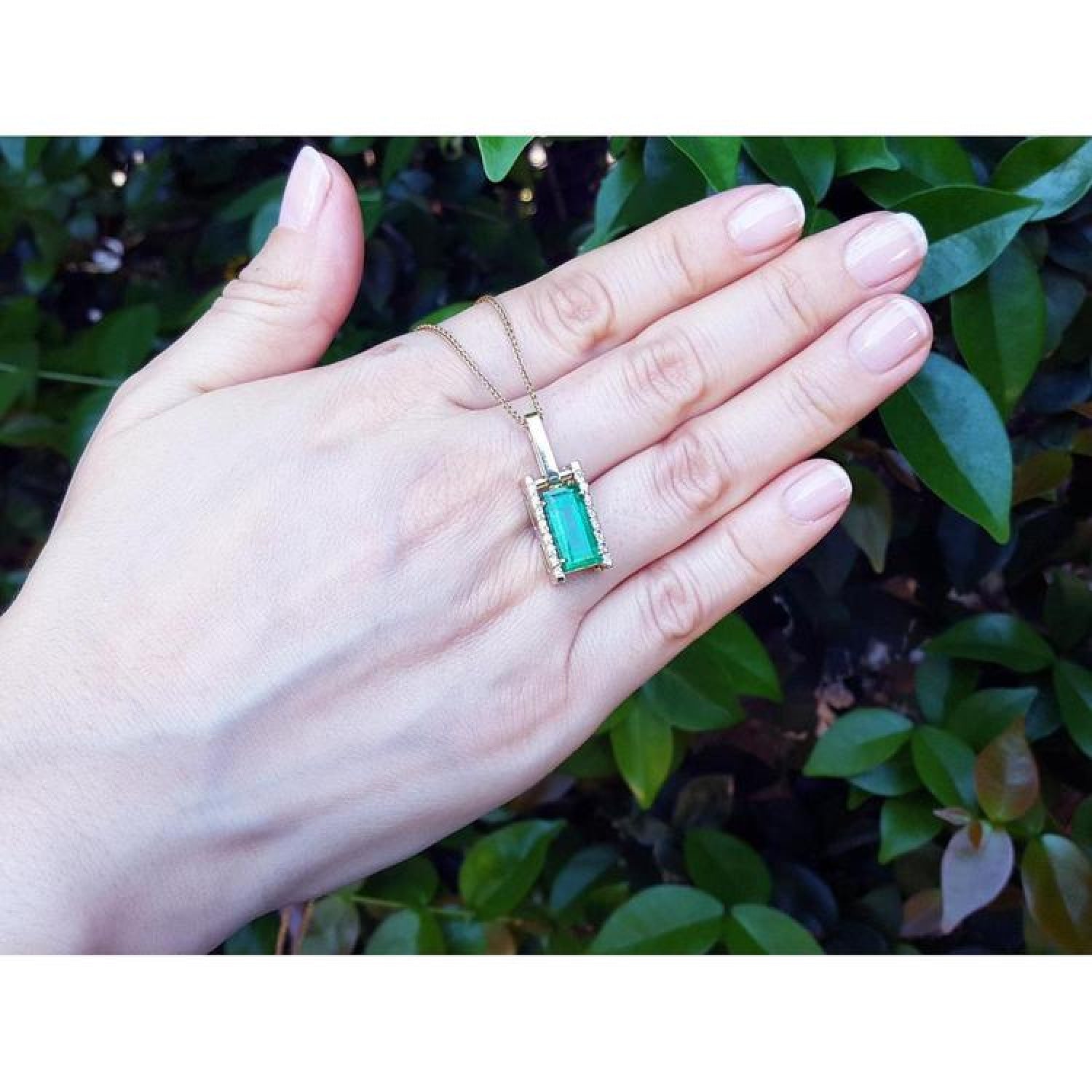 Baguette cut emerald pendant in 18K yellow gold with diamond accents, worn on a hand.