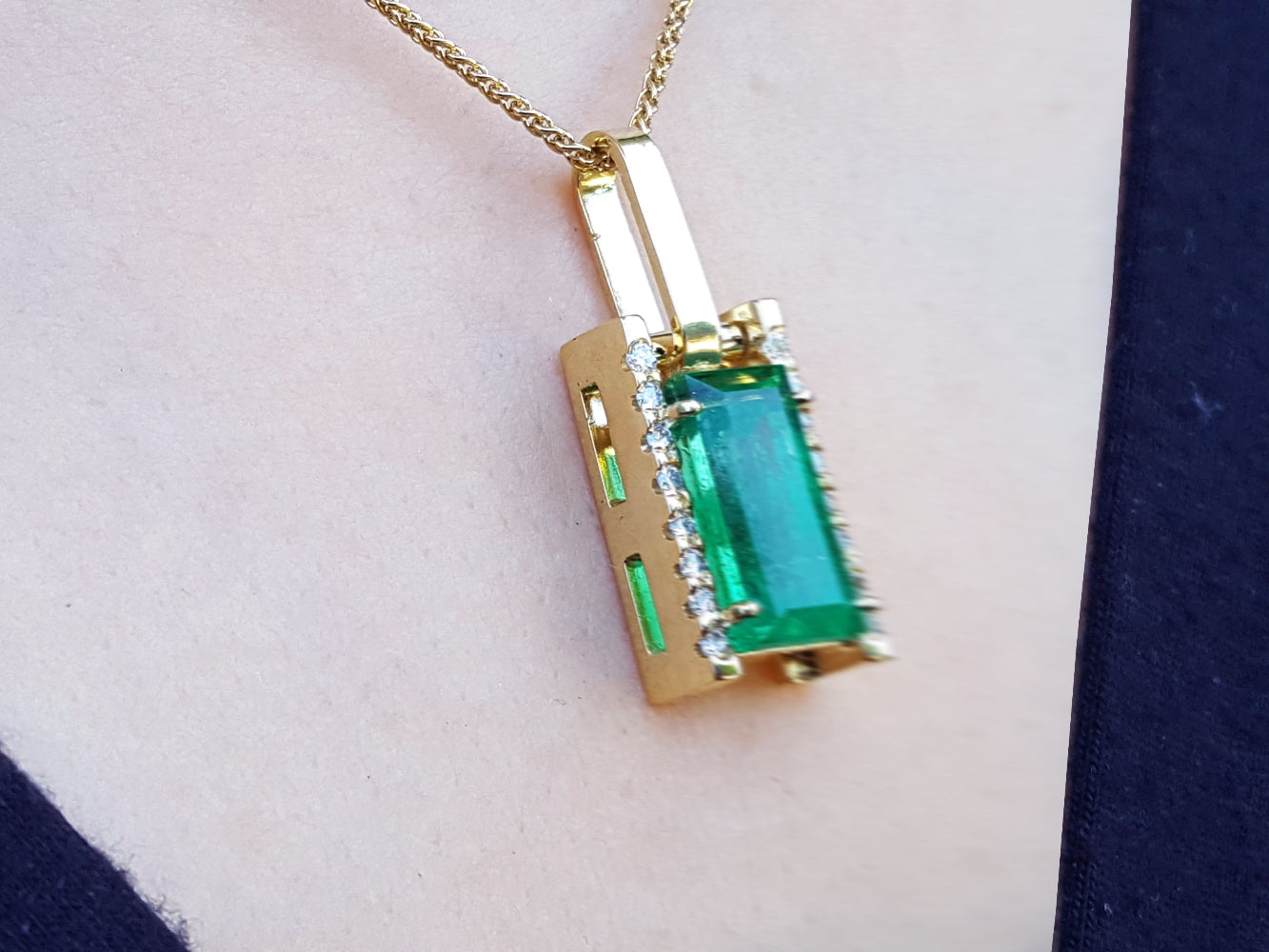 Gold pendant with a baguette cut emerald gemstone on a person's chest.