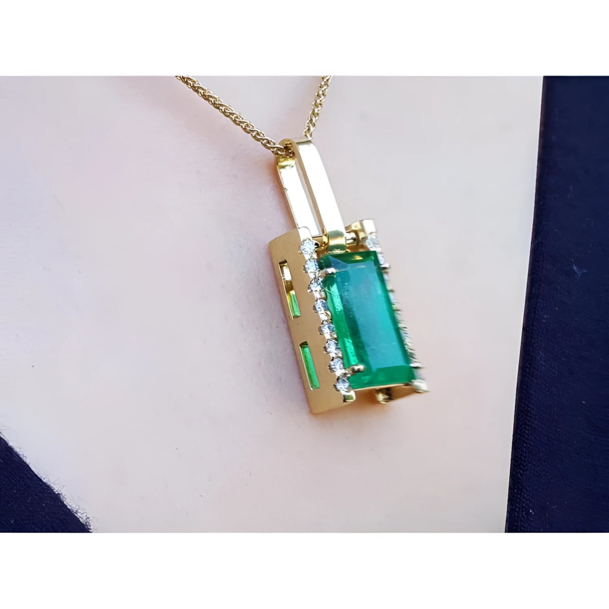 Gold pendant with a baguette cut emerald gemstone on a person's chest.