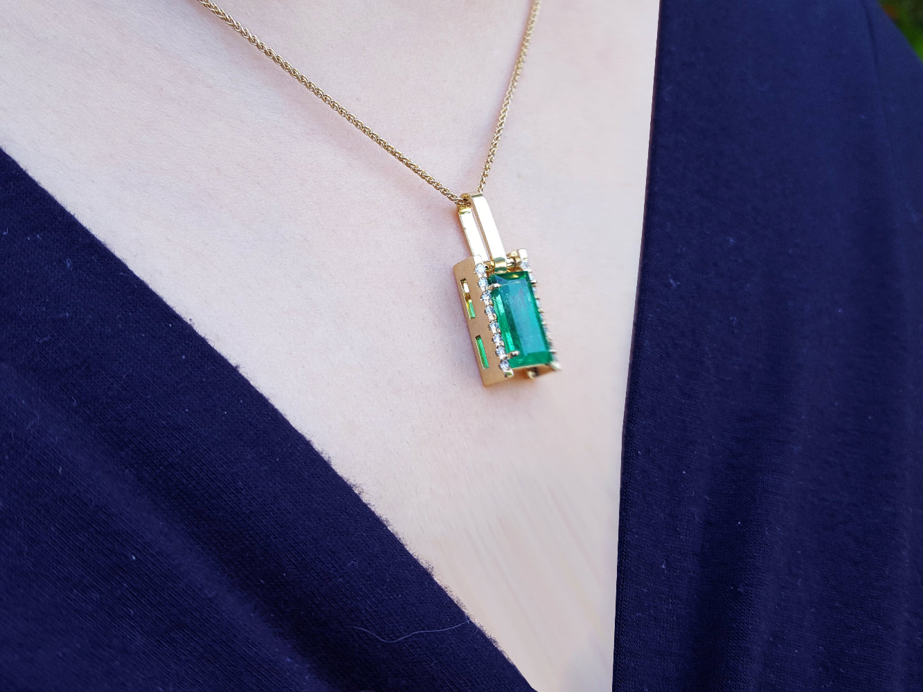 Gold necklace with a natural emerald pendant on a white and person&#39;s neck.