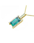 Baguette cut Colombian emerald pendant in 18K yellow gold with diamond accents on a delicate chain.