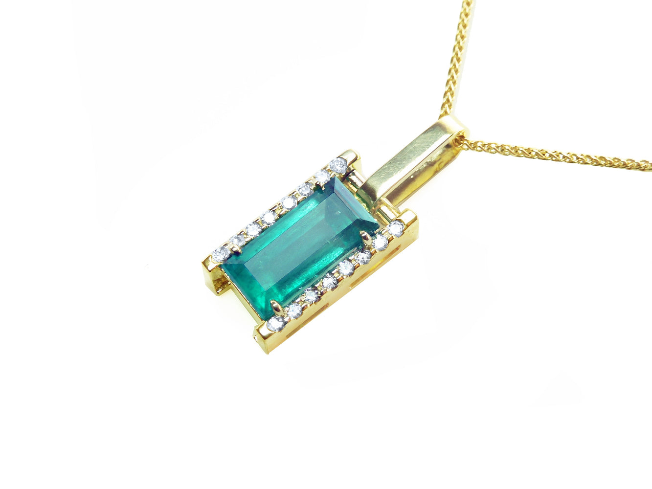 Te left side view of a baguette cut natural emerald pendant in yellow gold.