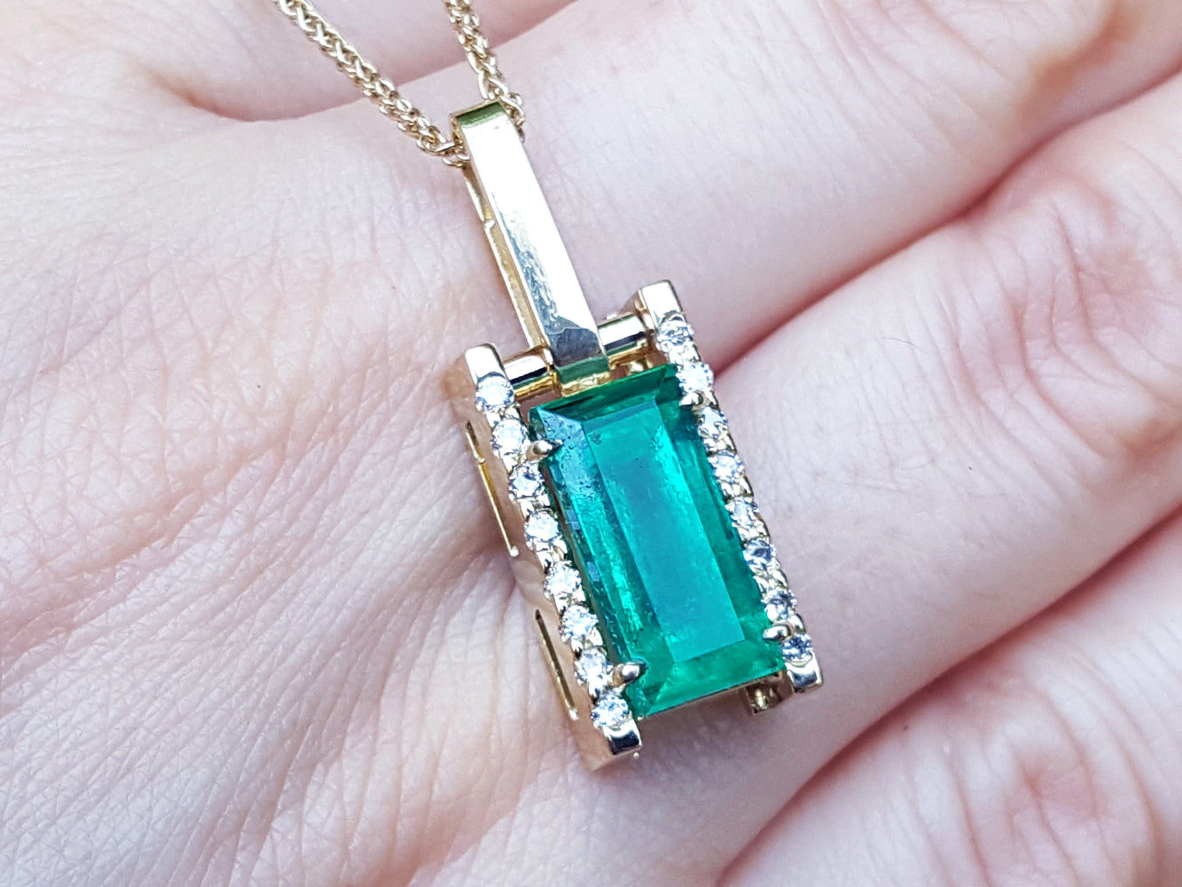Gold pendant with a baguette cut emerald held on hand.
