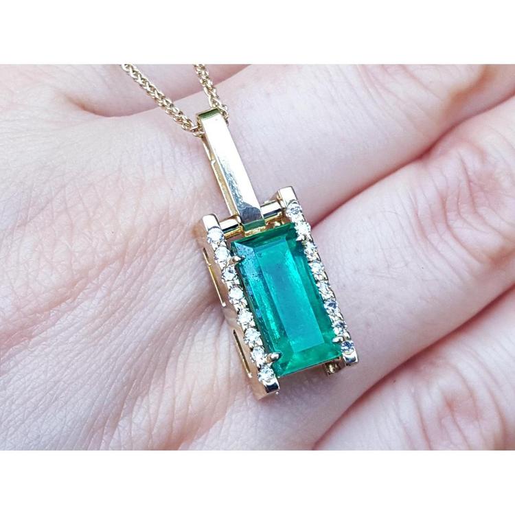 Gold pendant with a baguette cut emerald held on hand.