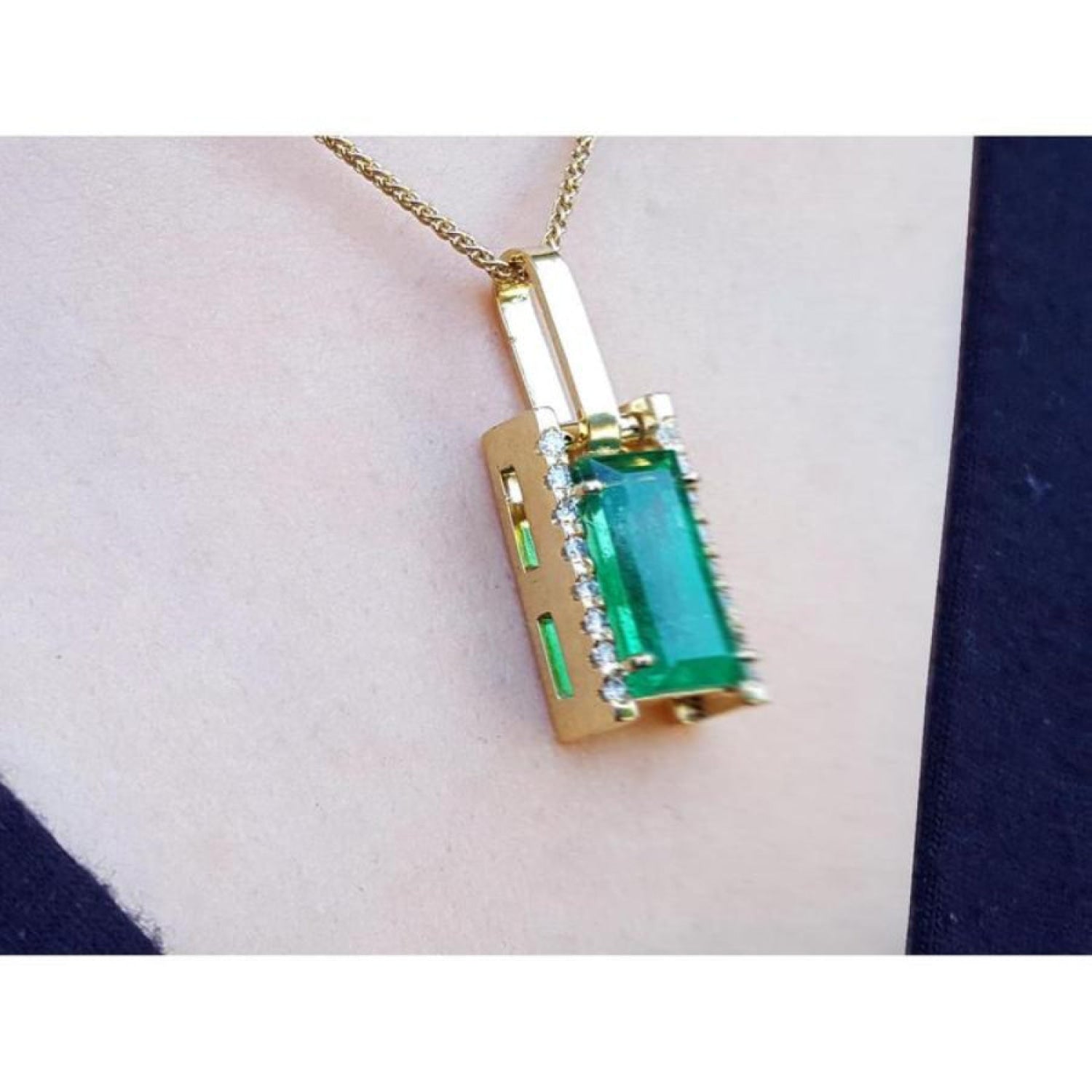 Gold pendant with a rectangular baguette cut natural colombian emerald gemstone on a person's chest.