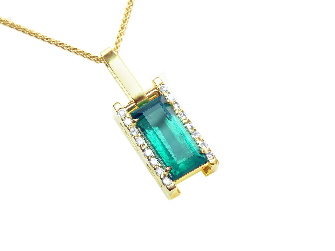 A yellow gold baguette cut emerald pendant with diamond accents topside view.