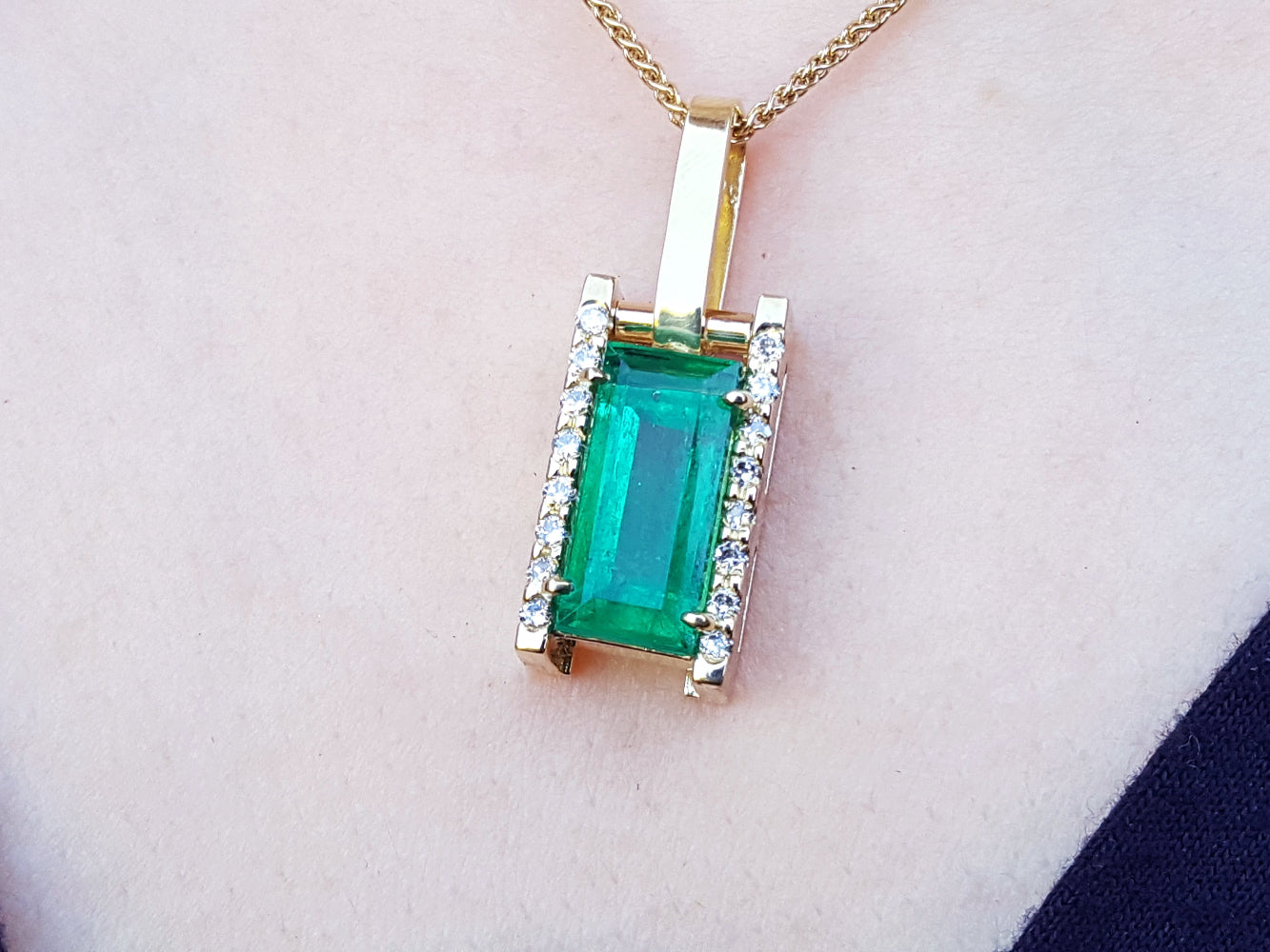 Gold pendant with a genuine emerald on a skin pink background.