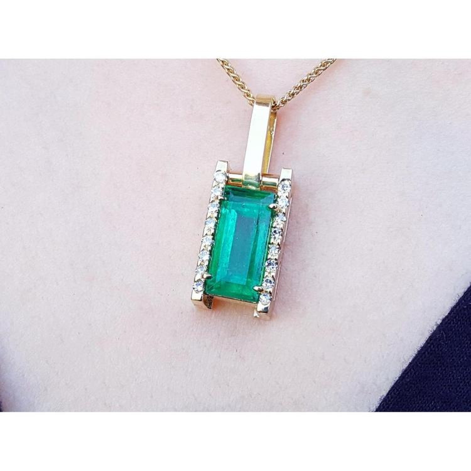 Baguette cut emerald pendant in 18K yellow gold with diamond accents, worn on a neck.