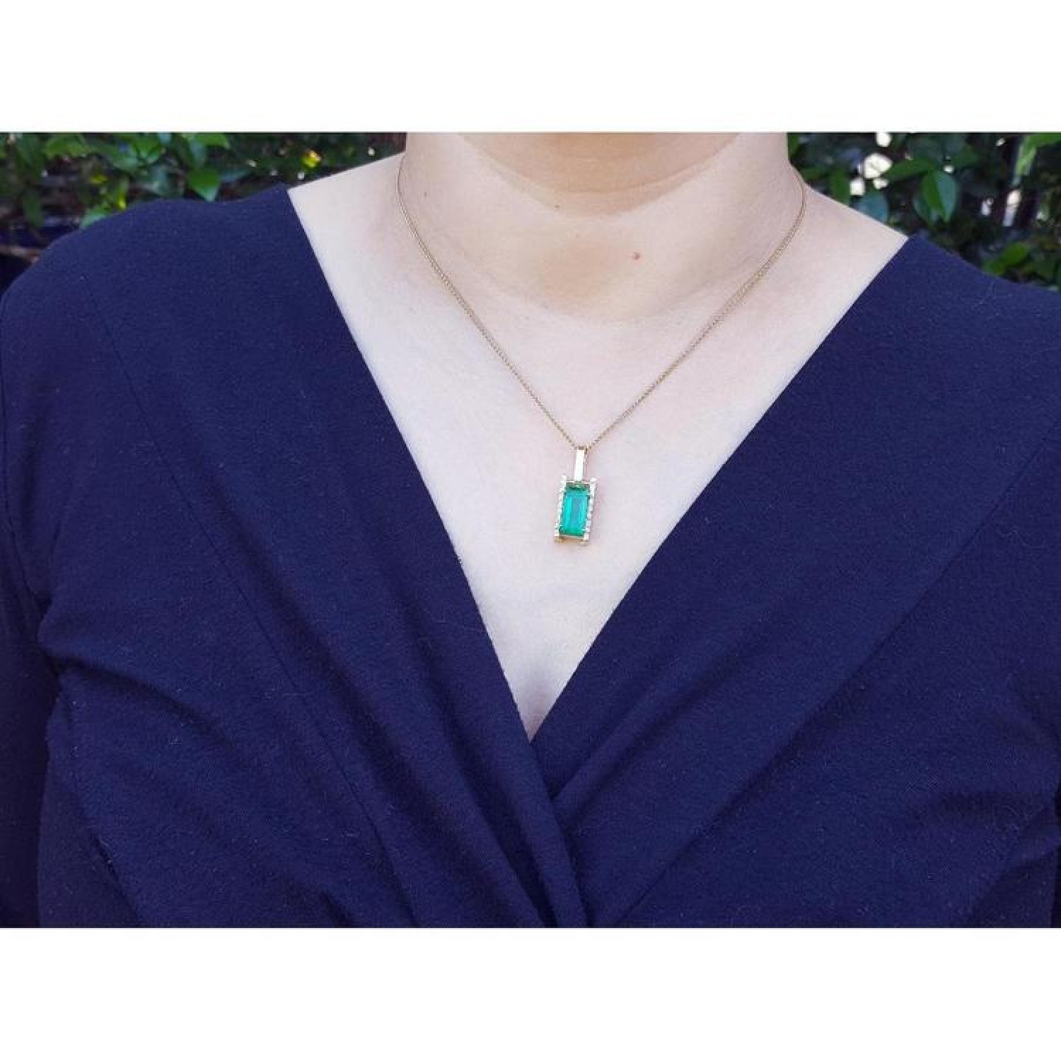 Baguette-cut Colombian emerald pendant in 18K yellow gold with diamonds, worn on a woman's neck.
