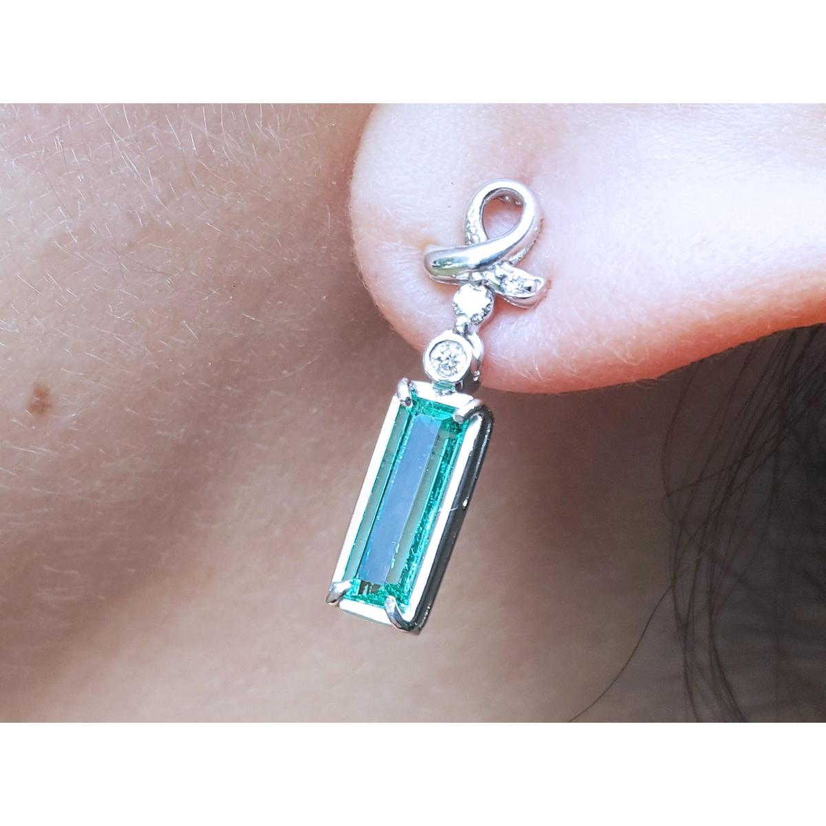 Natural baguette cut emerald earrings with a top ribbon-like worn by a person