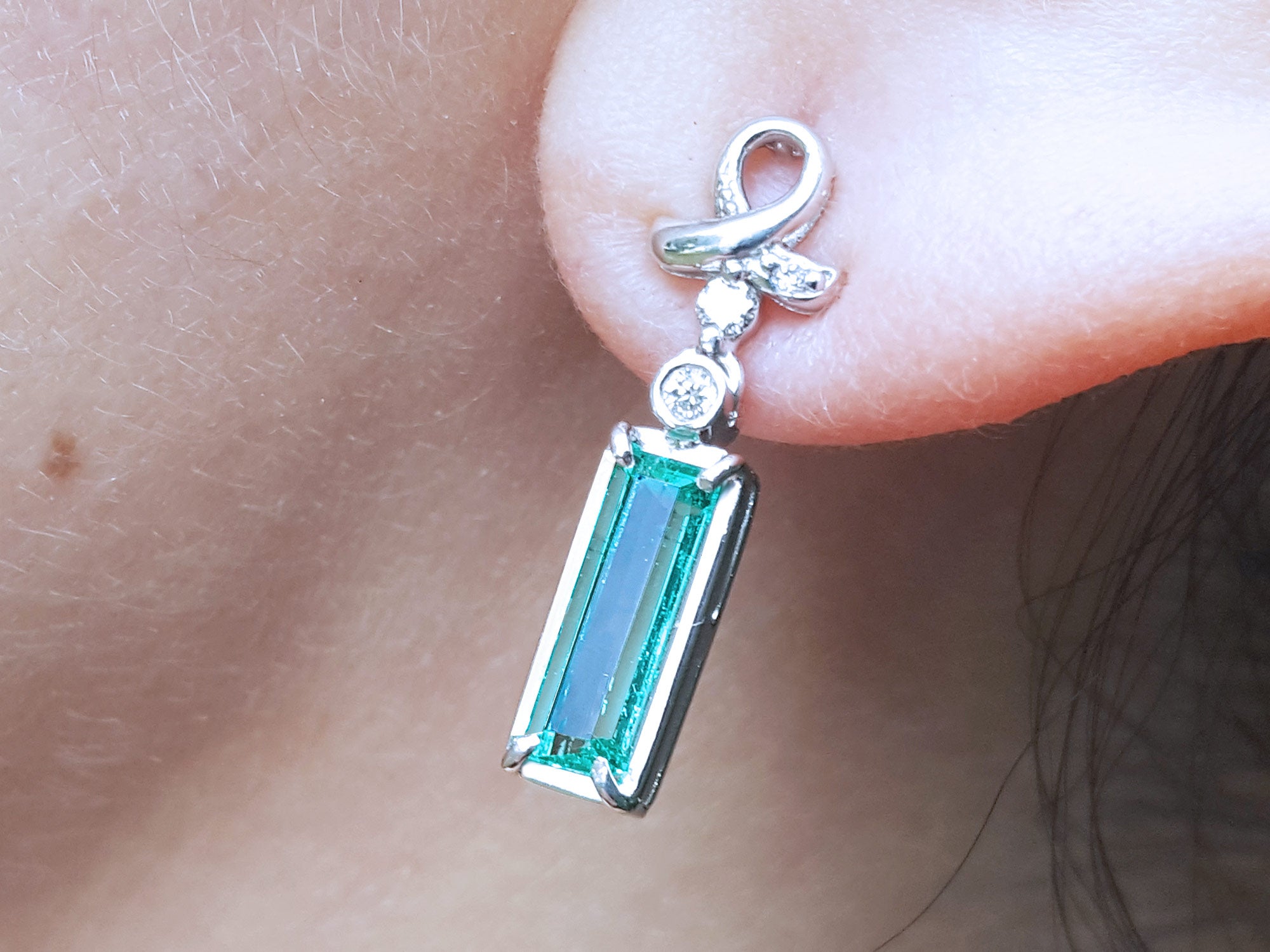 Natural baguette cut emerald earrings with a top ribbon-like worn by a person