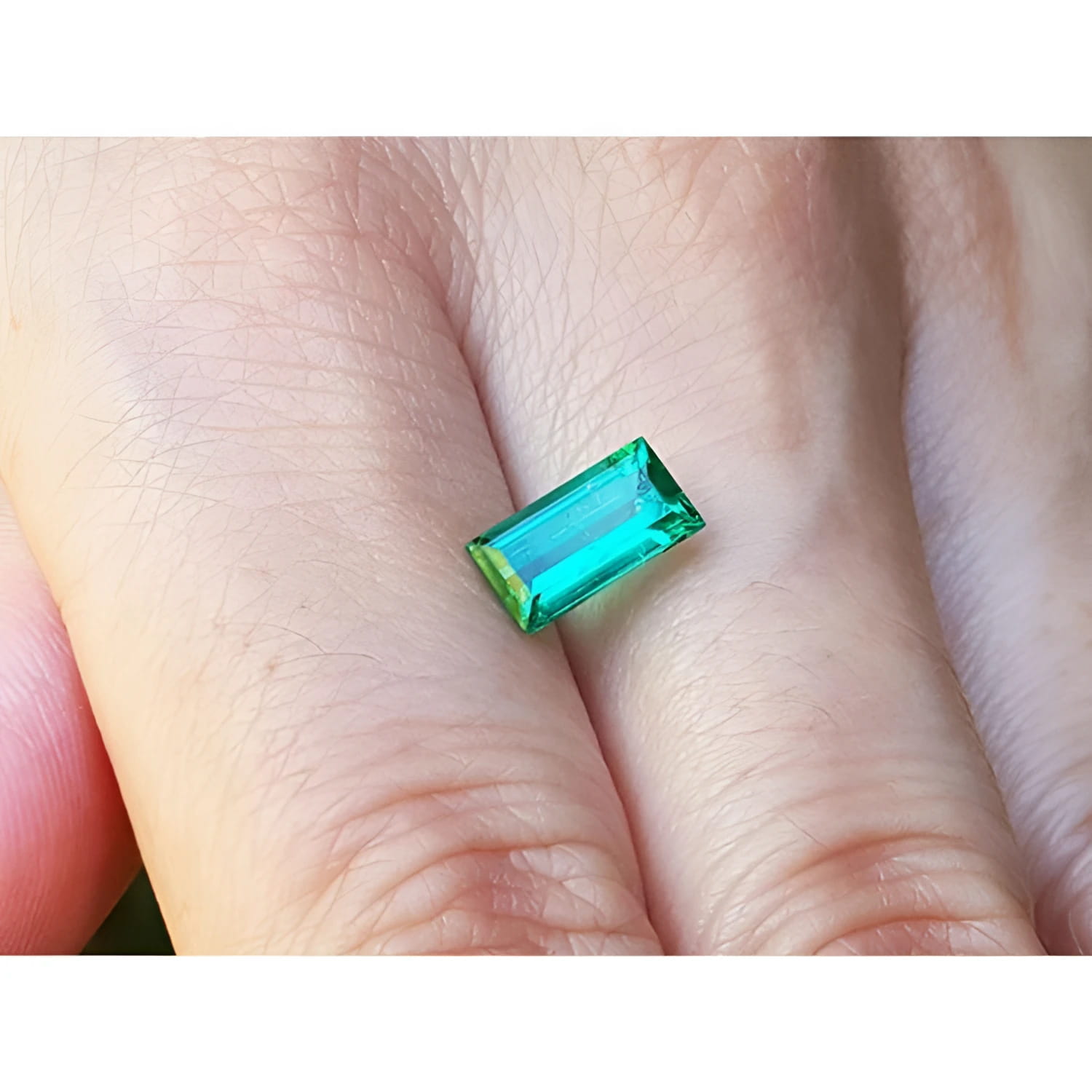 1.62 ct. baguette-cut loose natural emerald, vibrant green, held between fingers.