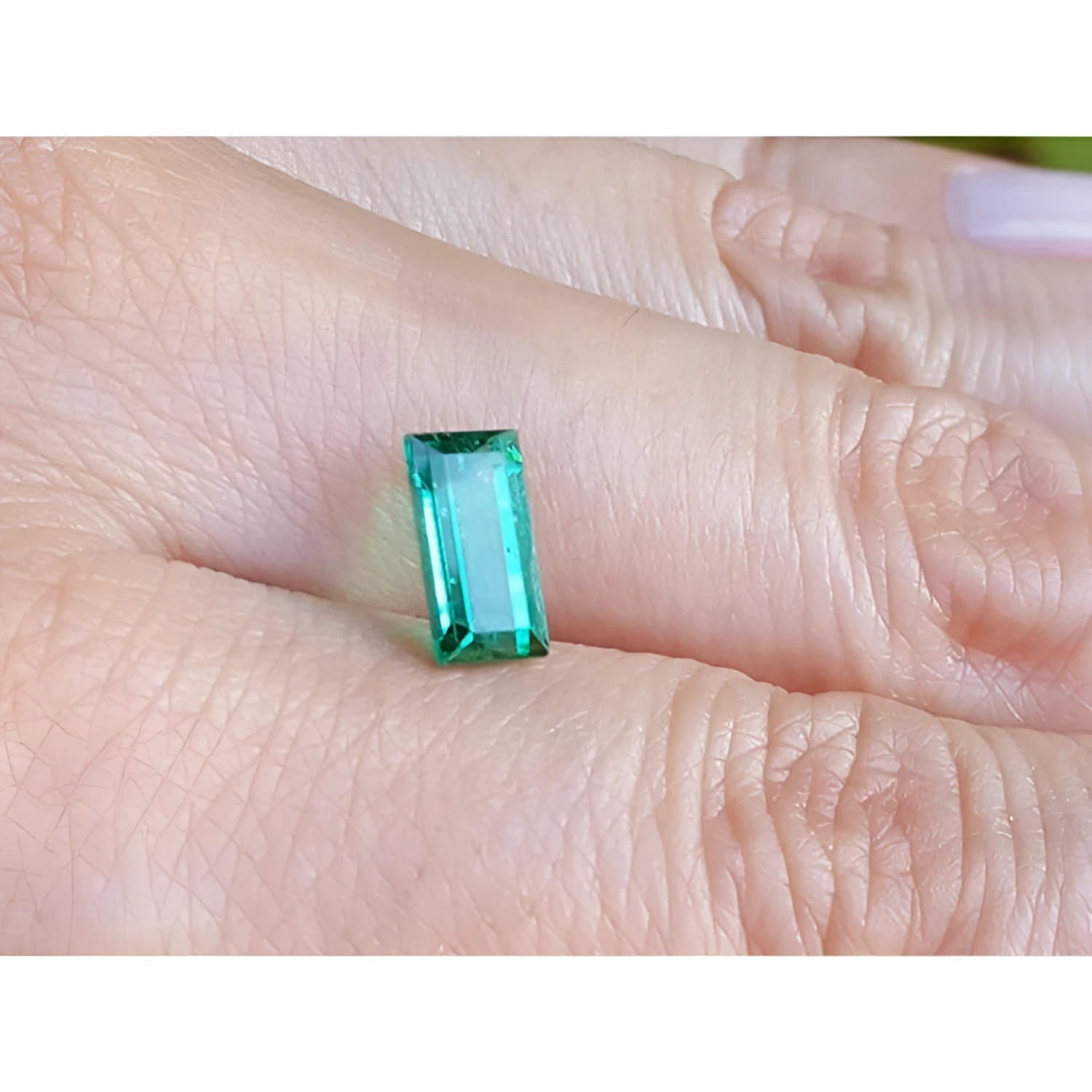 1.62 ct. baguette-cut loose natural emerald, vibrant green, held on a finger.