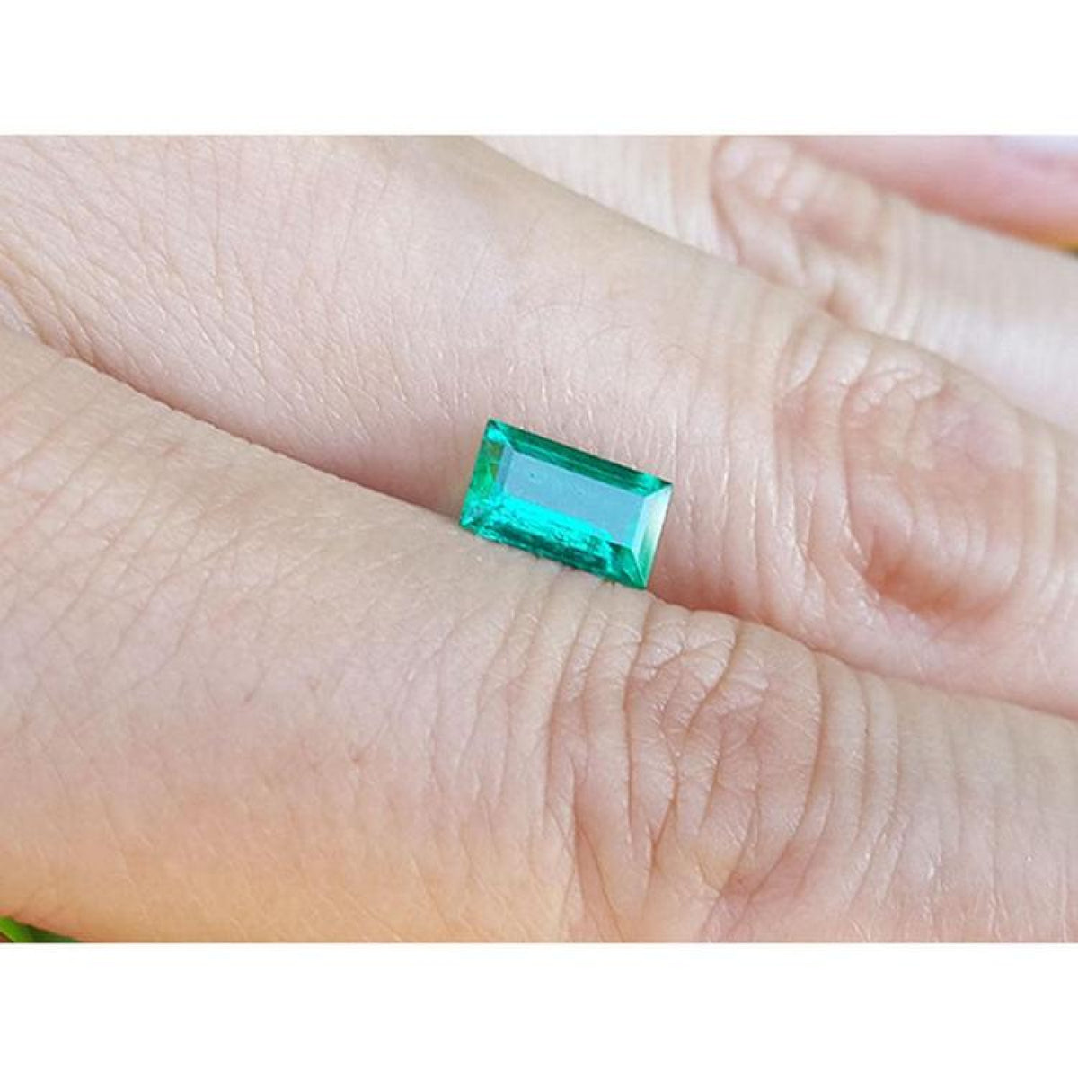 Vibrant green 1.10 ct. baguette-cut loose Colombian emerald gemstone held on a hand.