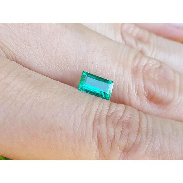 Vibrant green 1.10 ct. baguette-cut loose Colombian emerald gemstone held on a hand.