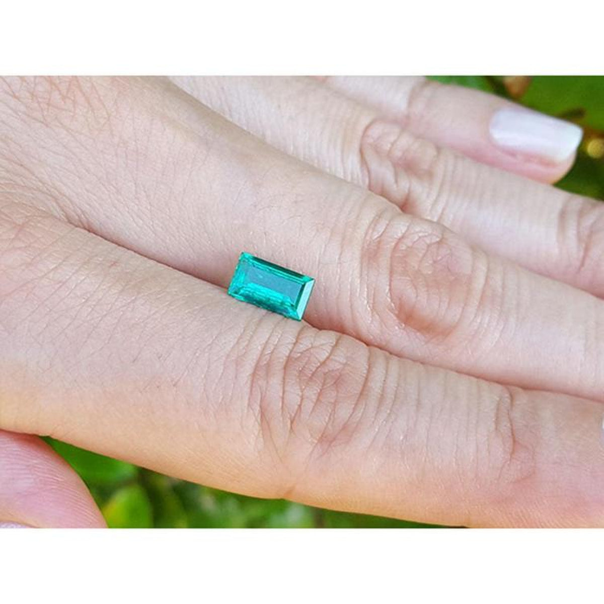 Vibrant green 1.10 ct baguette cut loose Colombian emerald held between two fingers.