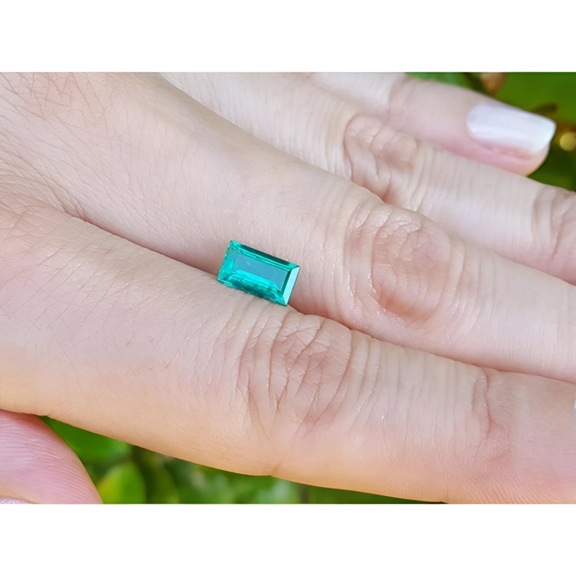 Vibrant green 1.10 ct baguette cut loose Colombian emerald held between two fingers.