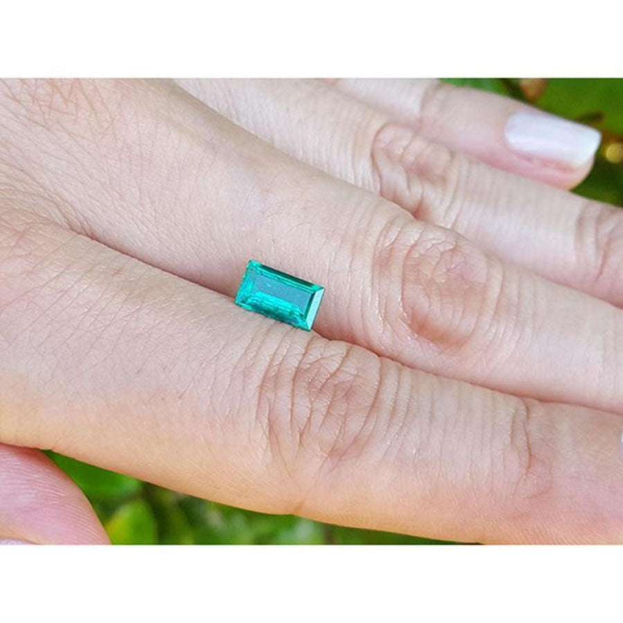 Vibrant green 1.10 ct baguette cut loose Colombian emerald held between two fingers.
