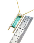 Emerald necklace for women yellow gold with a green baguette cut gemstone pendant next to a ruler for scale on a white background

