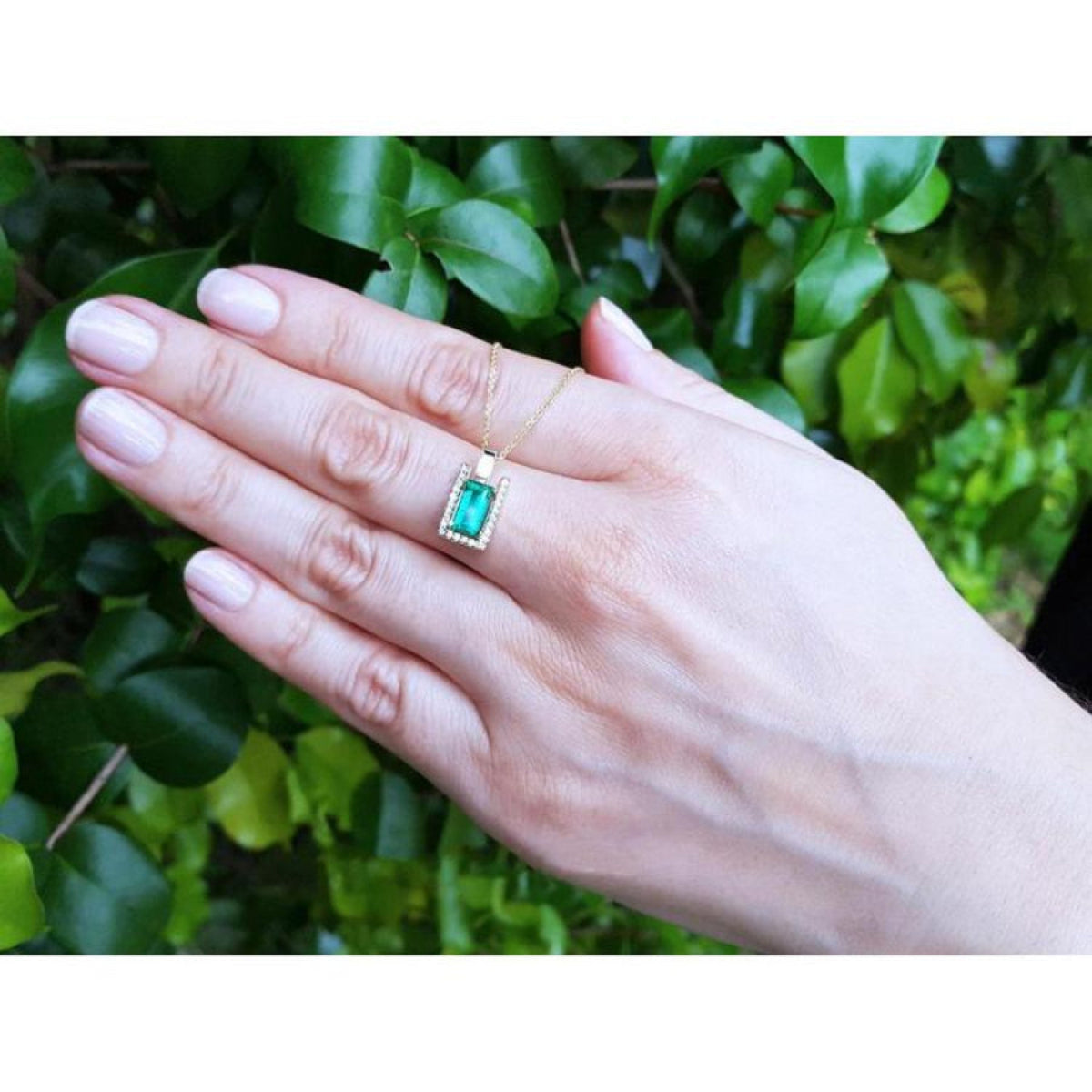 1.14 ct baguette emerald pendant necklace with diamond bail on a woman's hand, 14K yellow gold.