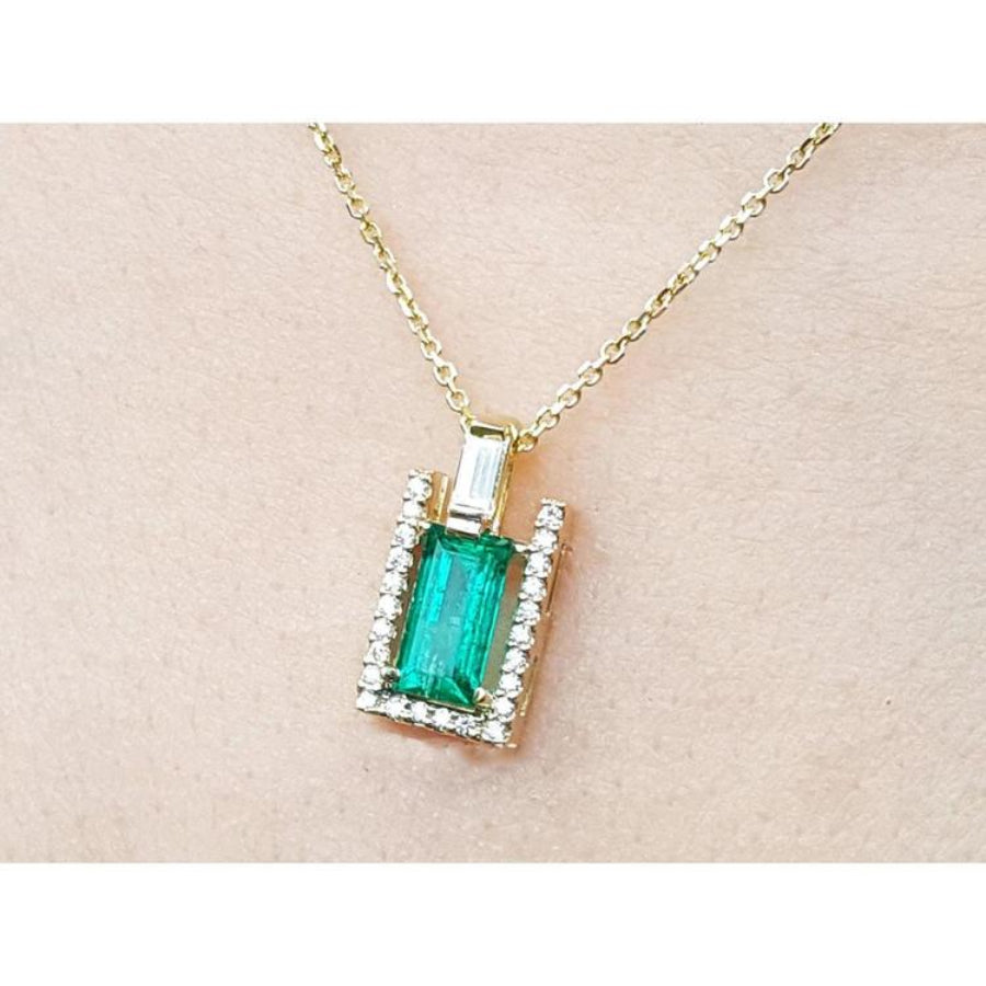Gold necklace with a baguette cut emerald pendant on a beige skin background.