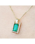 Gold necklace with a baguette cut emerald pendant on a beige skin background.