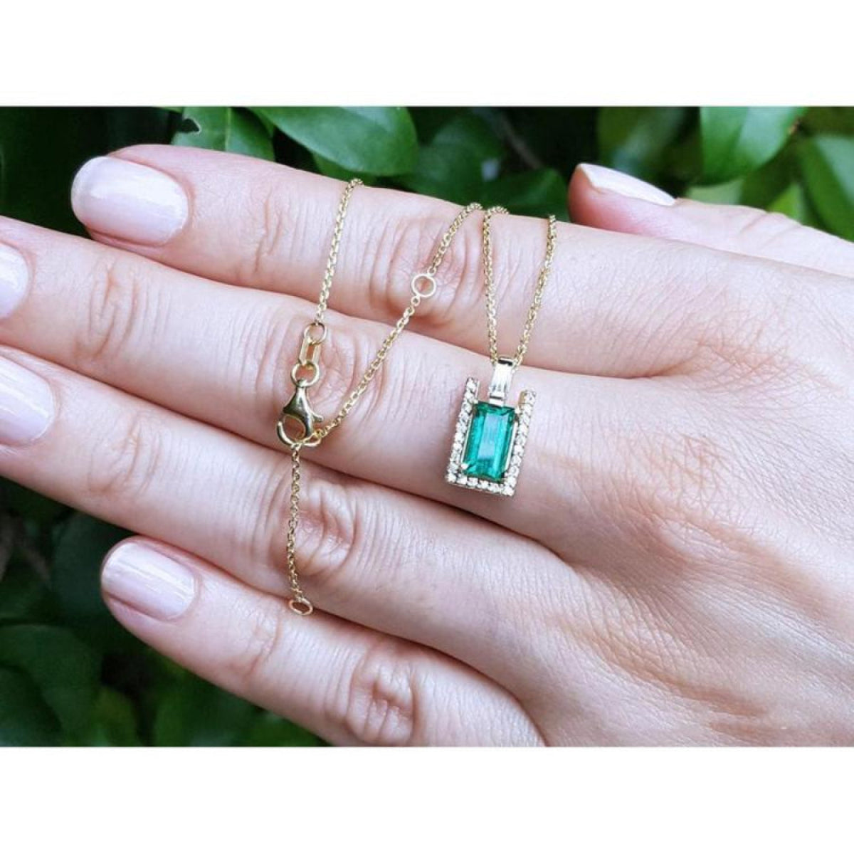 Baguette cut emerald pendant necklace with natural diamonds in 14K yellow gold, held in a hand.