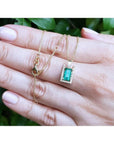 Baguette cut emerald pendant necklace with natural diamonds in 14K yellow gold, held in a hand.