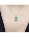 Baguette emerald and diamond pendant necklace in 14K yellow gold, worn on a neck.