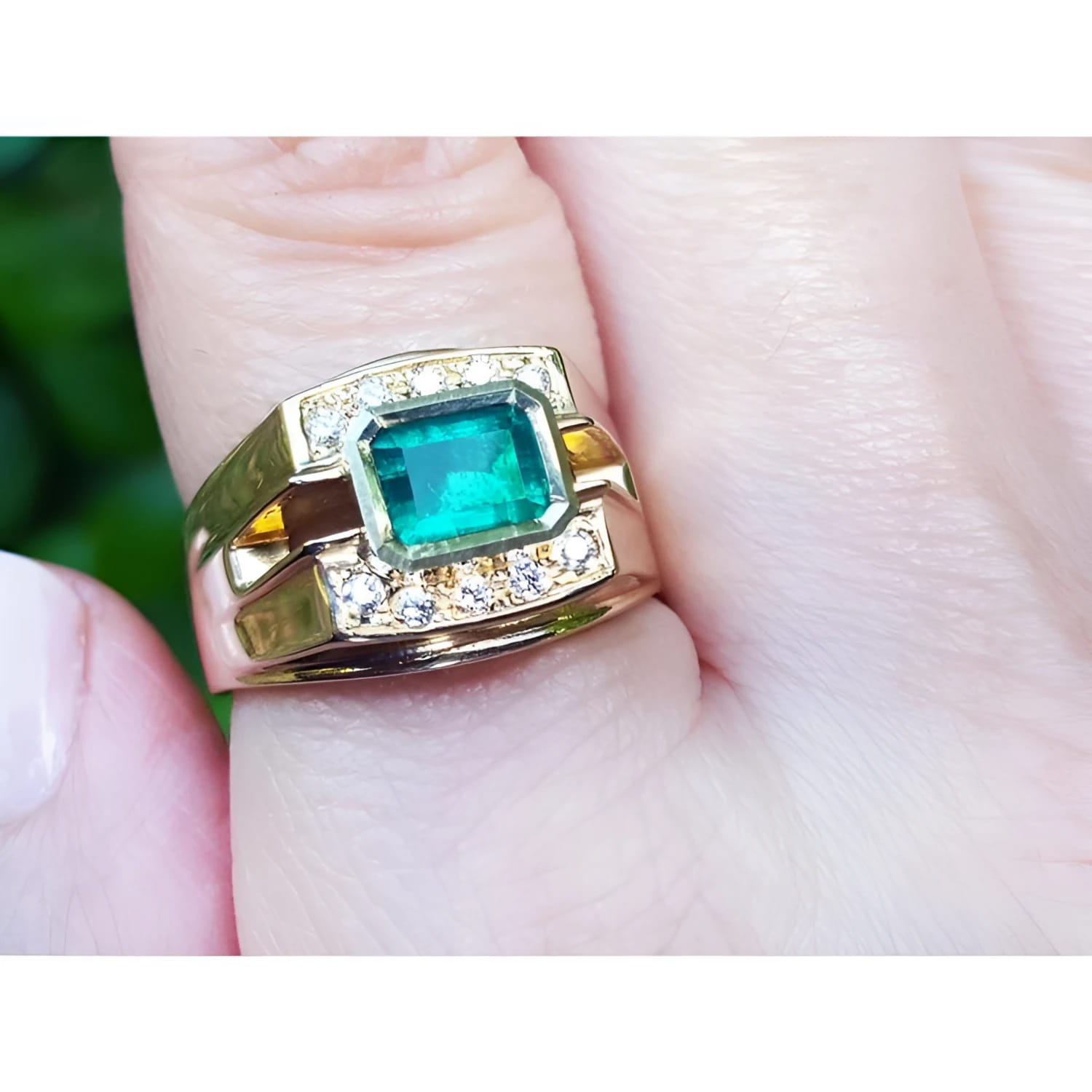 A 14k yellow gold natural colombian emerald ring for men with accent diamonds worn on a finger.