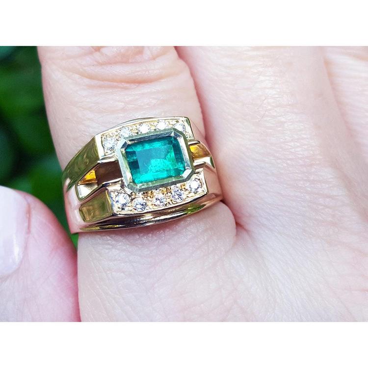 A yellow gold mens natural emerald ring with accent diamonds on a finger.