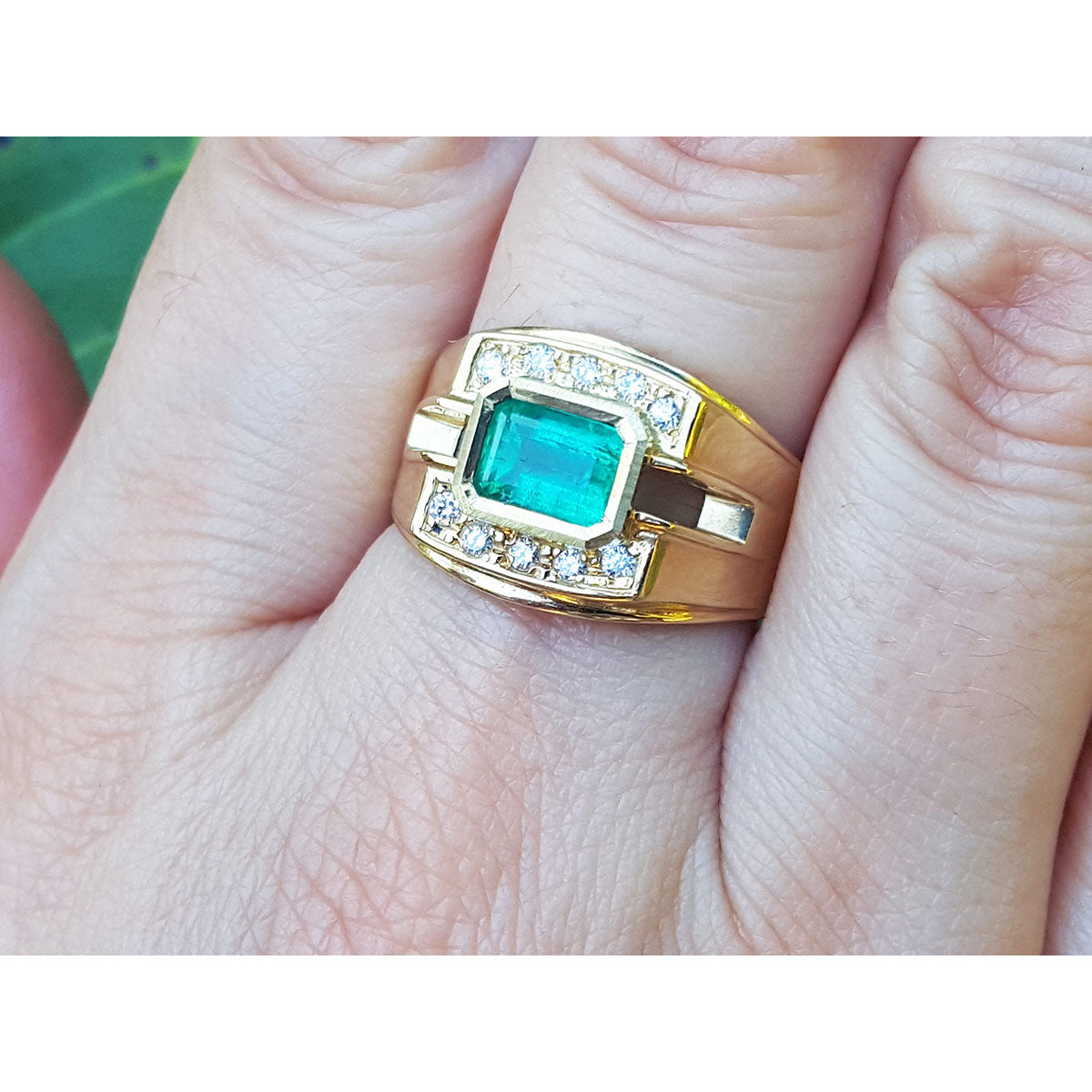 East west style emerald ring for men in yellow gold on a person&#39;s finger.