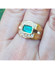 East west style emerald ring for men in yellow gold on a person's finger.