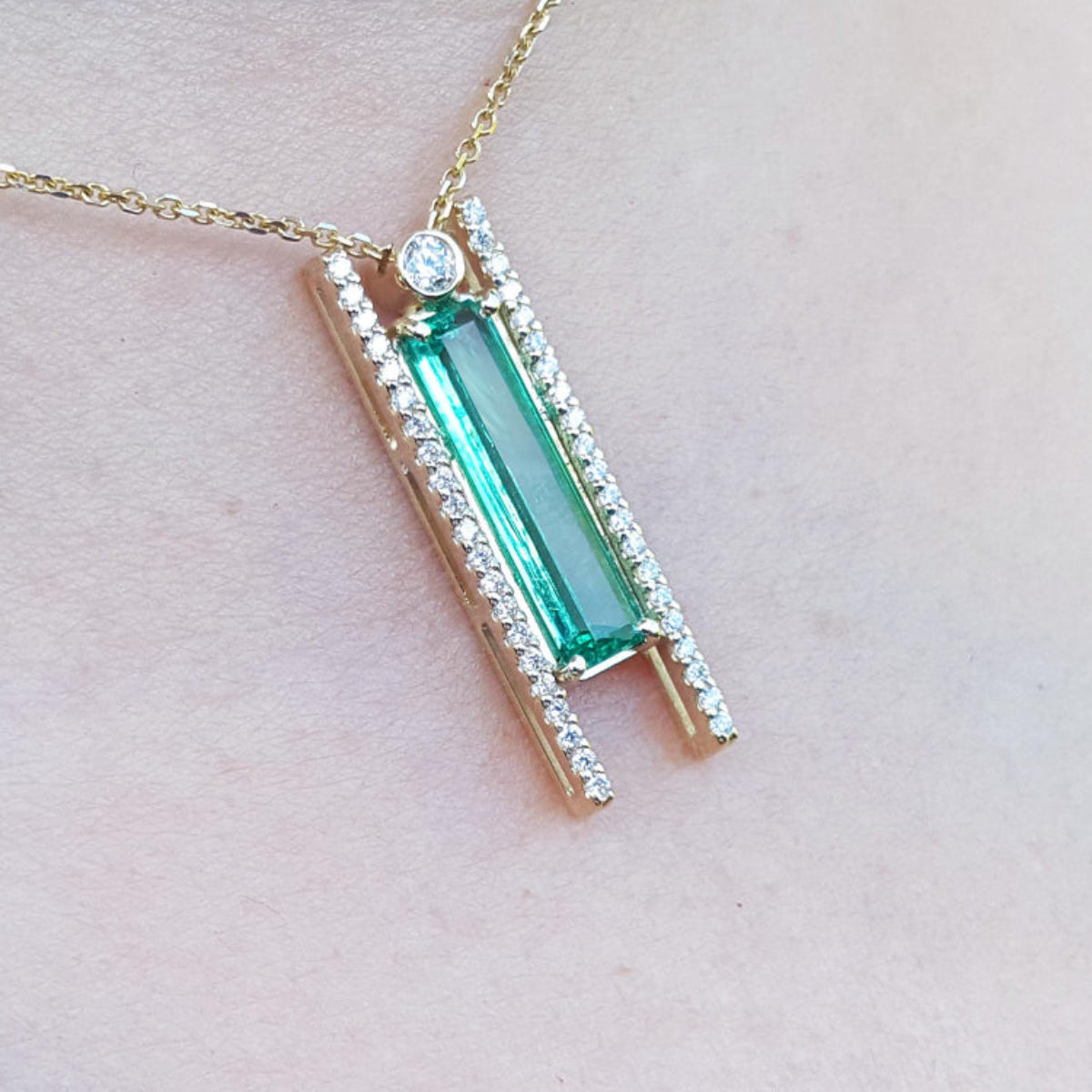 Zoom-in of a yellow gold baguette cut emerald necklace and small side diamonds on a woman&#39;s neck
