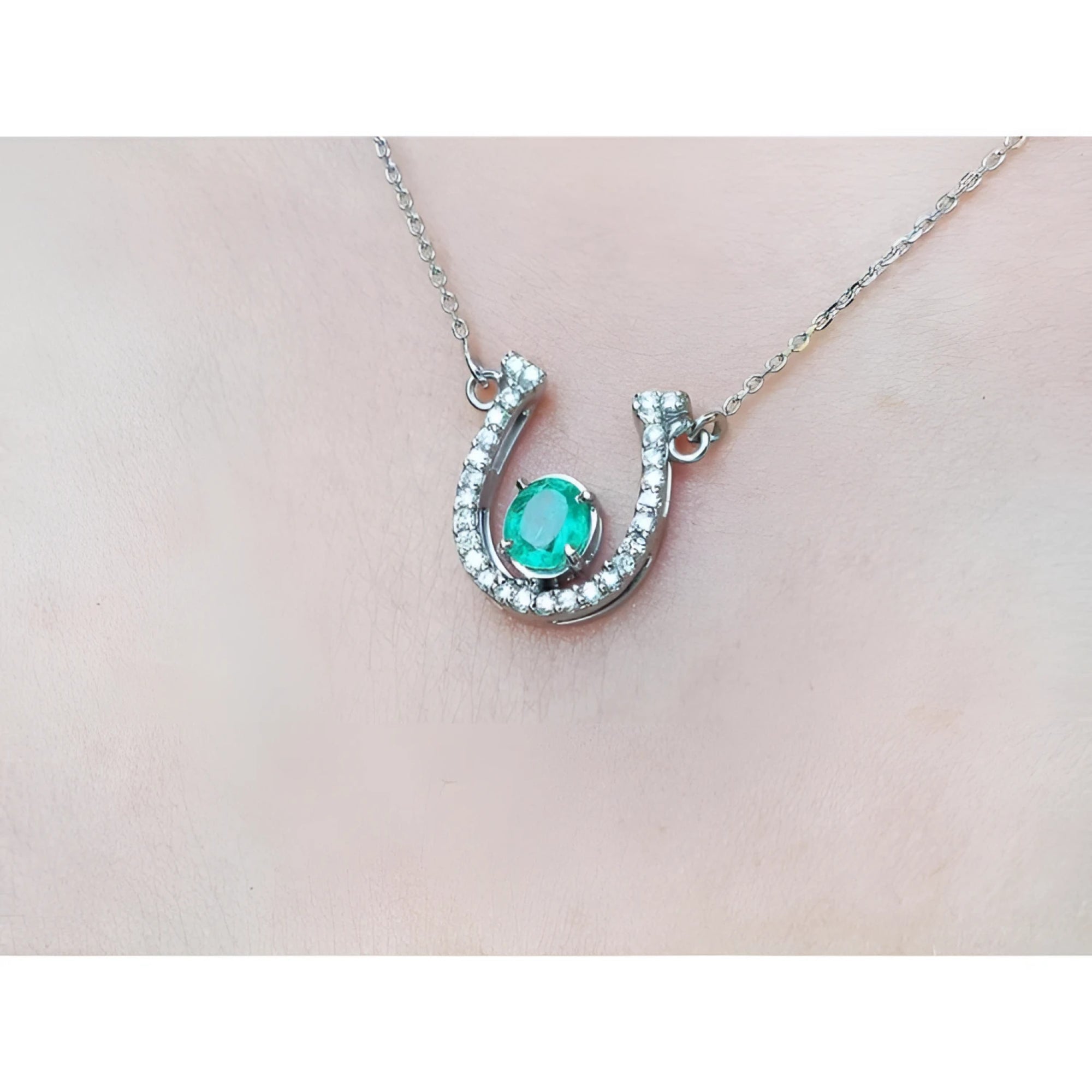 14K white gold horseshoe necklace with a prong-set oval emerald and natural diamonds.