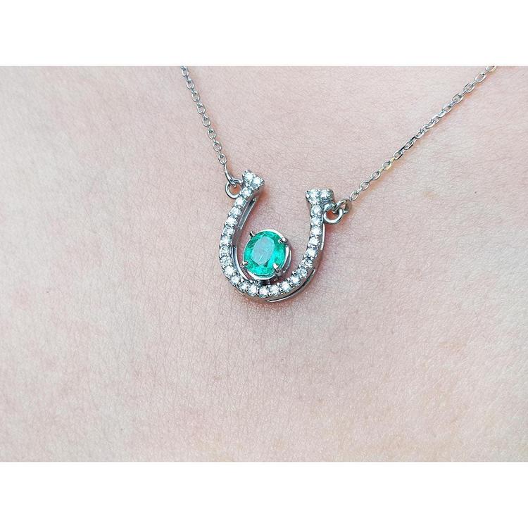 14K white gold horseshoe necklace with a prong-set oval emerald and natural diamonds.