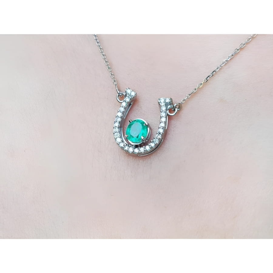 14K white gold horseshoe necklace with a prong-set oval emerald and natural diamonds.